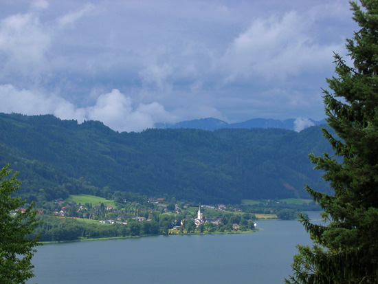 Grote slierten wolken drijven over de Ossiacher See voorbij. Slechts hier en daar is er een blauw plukje lucht waar te nemen, maar gelukkig probeert de zon de wolken met krachtige stralen op te lossen.